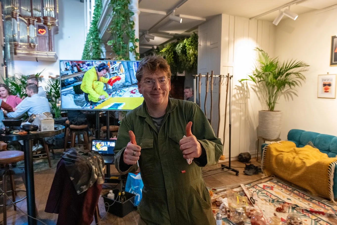 Ward Schepman tijdens een eerdere livepaintingbijeenkomst, met bezoekers en een kleurrijk werk achter hem.